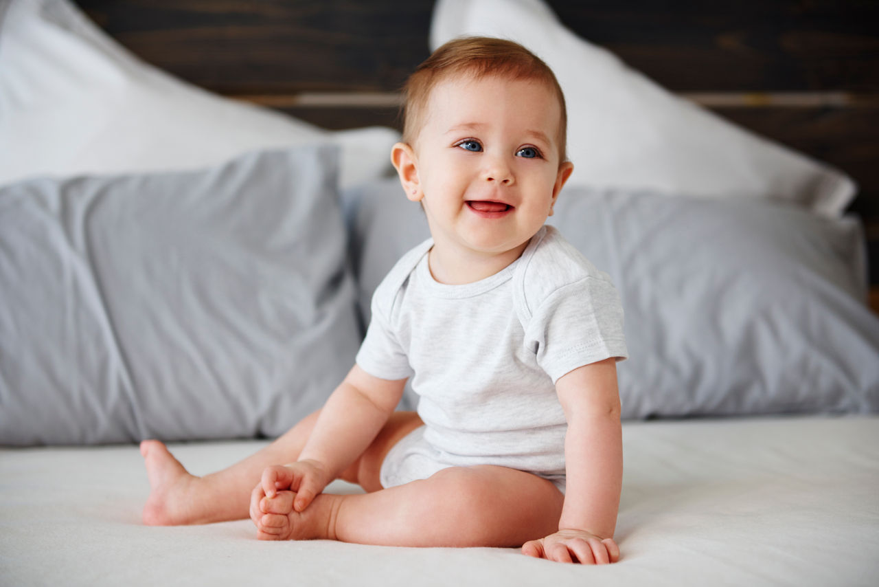 Baby sitzt im Bett lachend