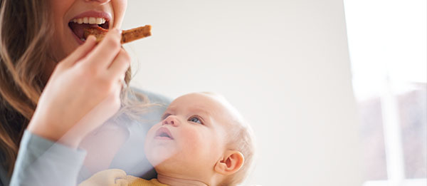 Mutter isst mit Baby auf dem Arm