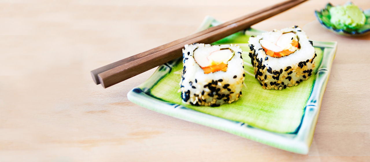 Zwei Sushi-Rollen auf einem kleinen Teller mit Essstäbchen